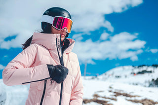 Woman in pink ski jacket, black helmet and goggles outdoors on snowy mountain