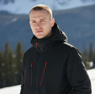 Man wearing a black winter jacket with red zippers in snowy mountain setting