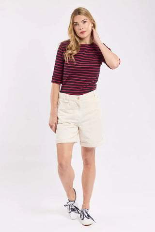 Woman in navy and red striped shirt, cream shorts, and white sneakers on white background