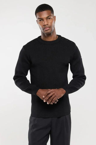 Man wearing a black knit crewneck sweater with shoulder buttons, posing against a white background