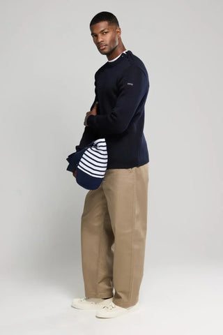 Man wearing a navy blue sweater, beige pants, and white sneakers holding a striped shirt.