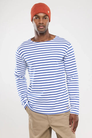 Man wearing a white and blue striped long sleeve shirt, rust beanie, and beige pants