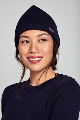 Woman wearing a navy blue wool Breton beanie and sweater, close up, neutral background