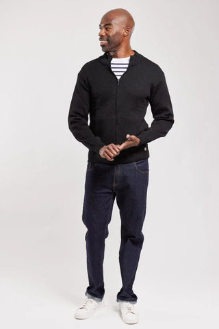 Man wearing a black zip-up wool cardigan, striped shirt, dark jeans, and white sneakers
