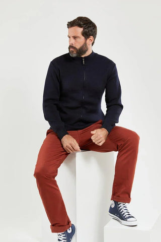 Man wearing a navy zip wool cardigan, rust pants, and blue high-top sneakers, seated indoors