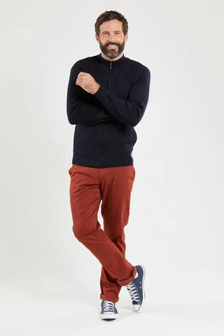 Man in navy zip cardigan, rust pants, and blue sneakers on white background