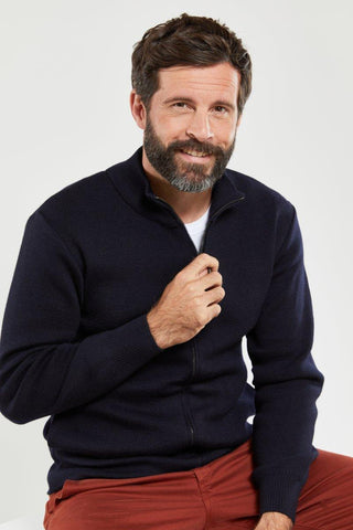 Man wearing a navy wool zip cardigan and red pants on a neutral background