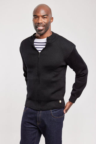 Man wearing a black wool zip-up cardigan over a striped shirt and dark jeans