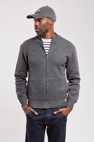 Man wearing a grey zip-up wool cardigan over a striped shirt with a cap and jeans