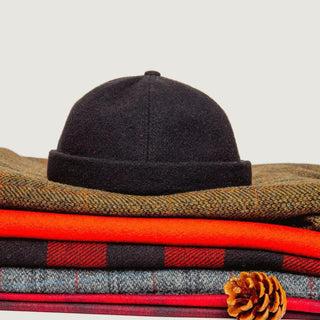 Black wool beanie on folded winter sweaters with pinecone accent