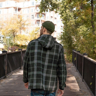 Man in green wool beanie and plaid jacket walking on a wooden bridge in autumn