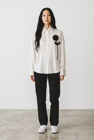 Blouse Le Capitaine D'a Bord blanche à manches longues avec une fleur noire appliquée sur la poitrine