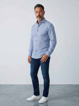 Homme portant une chemise Le Capitaine D'a Bord bleue à motifs, coupe moderne, avec un jean et des baskets blanches.