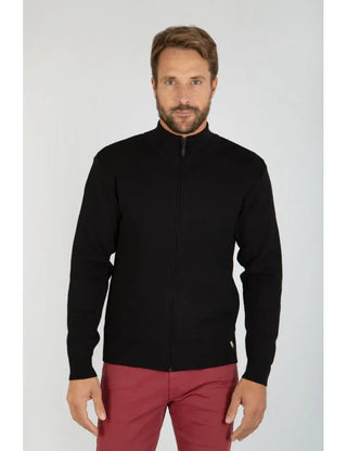 Man wearing a black zip wool cardigan and red pants on light background