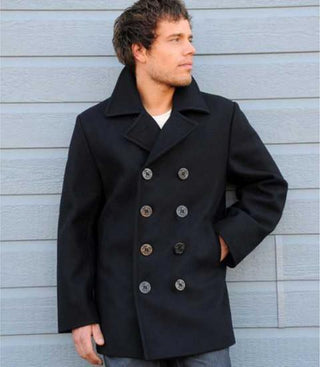 Man wearing a navy wool pea coat with double-breasted buttons, standing against a gray wall.