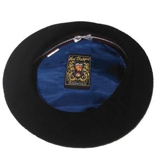 Interior of a black Basque beret with blue lining and embroidered label visible.
