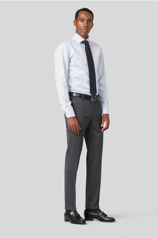 Man wearing light grey wool dress pants, white shirt, navy tie, and black loafers, standing indoors