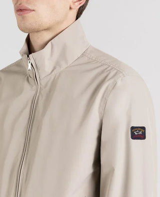 Beige men's nylon jacket with high collar, zip closure, and logo patch on the sleeve.
