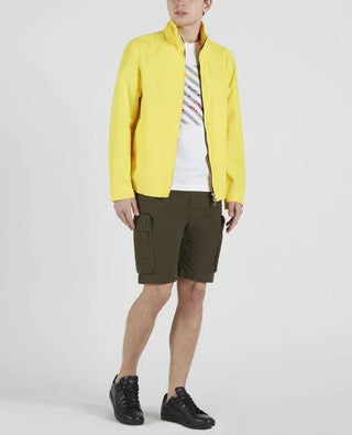 Man wearing yellow nylon jacket, white graphic T-shirt, olive cargo shorts, black sneakers