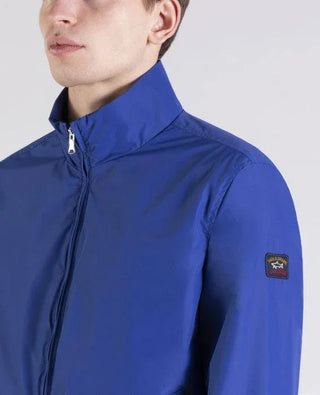 Man wearing a blue nylon zip-up jacket with patch logo on sleeve