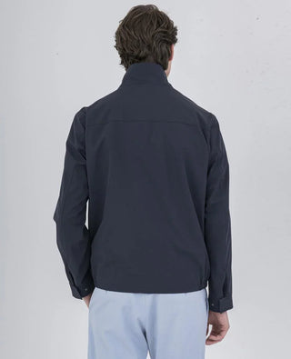 Man wearing navy nylon jacket with high collar and light blue pants, shown from the back