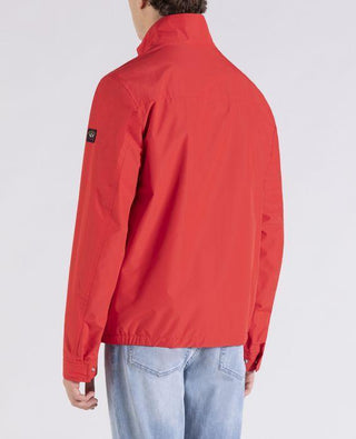 Back view of a man wearing a red nylon jacket with light blue jeans, casual style