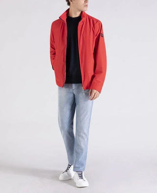 Man in red nylon jacket, light blue jeans, white sneakers, casual fashion style