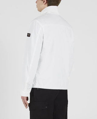 Man wearing a white nylon jacket with badge on sleeve and black cargo pants, back view