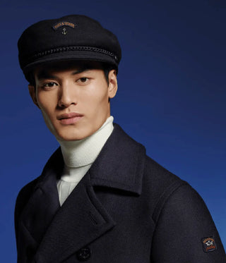 Man wearing a navy wool sailor cap and pea coat against a blue background