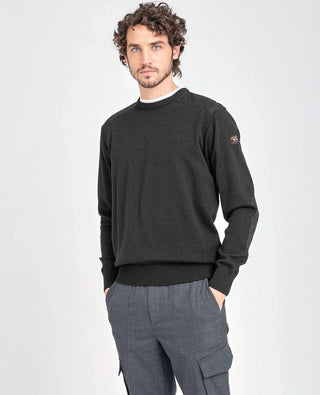 Man wearing a black crew neck sweater with shoulder patches and grey trousers