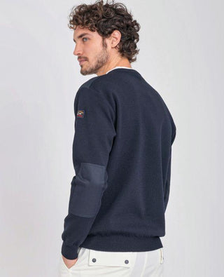 Man wearing navy crew neck sweater with shoulder patches and white pants, back view