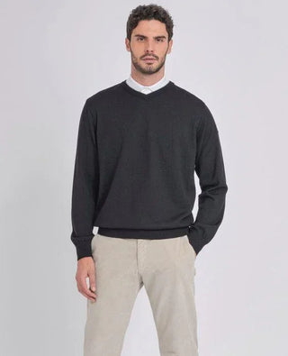 Man wearing a black merino wool V-neck sweater and beige pants against a plain background