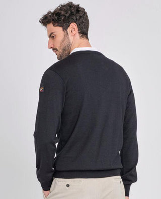 Man wearing a black V-neck merino wool sweater and beige pants, seen from the back.