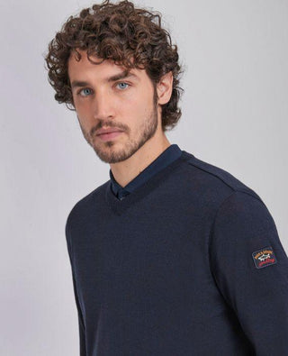Man wearing navy merino wool V-neck sweater with patch on sleeve, neutral background