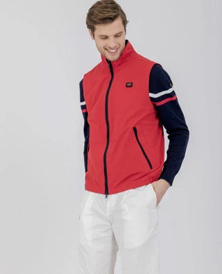 Man wearing red sleeveless nylon vest with zip front, navy sleeves, white pants, casual style