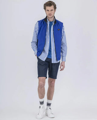 Man wearing blue sleeveless vest, striped shirt, denim shorts, white sneakers, and striped socks