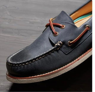 Men's navy leather boat shoe with brown laces and white non-slip sole close-up